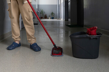 Cleaning floors with a mop and bucket in a hallway setting during the day