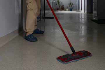 Person mopping a clean floor in a modern hallway during daylight hours
