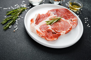 Uncooked beef steaks on white plate with rosemary and spices