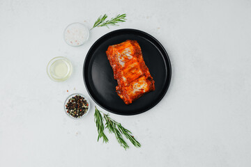 Spicy pork ribs on black plate with seasoning and herbs