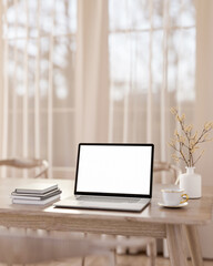 Blank screen laptop with coffee and books aside vase on wooden table across window and sheer curtain