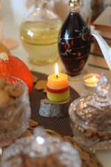 Lit candles, cookies, chocolate, nuts, tea, wine, pumpkins, books, reading glasses and autumn leaves on the table. Autumnal hygge at home. Selective focus.