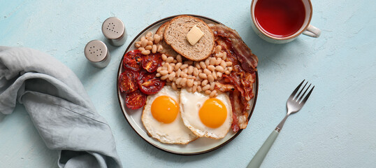 Plate with tasty English breakfast and cup of tea on blue background