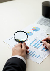 Businessman analyzing data with magnifying glass on charts and graphs  