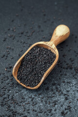 Wooden scoop filled with black sesame seeds on dark background