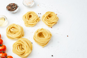 Raw tagliatelle pasta nests with tomatoes and spices on white background