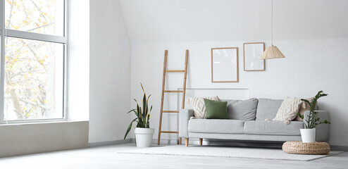 Interior of light living room with grey sofa, ladder and blank frames