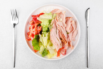 Protein salad with turkey, cheese and vegetables in white bowl with cutlery for fitness meal plan or diet food concept