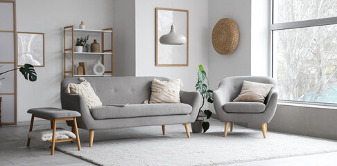 Interior of light living room with grey sofa, armchair and soft bench