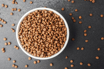 White bowl filled with dry dog food on black background with scattered kibbles