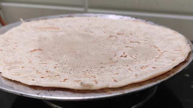 Closeup shot of traditional Indian jowar roti or sorghum flatbread being roasted on a pan over a gas stove with selective focus.