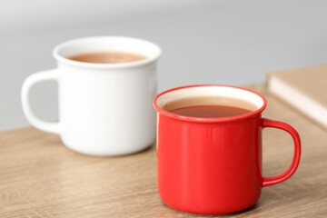 White and red mugs of hot tea on wooden table. Closeup