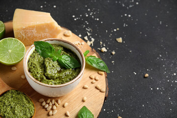 Bowl of delicious pesto sauce with ingredients on black grunge background