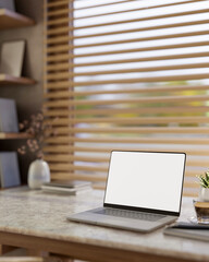 Fototapeta premium White screen laptop with book and coffee on marble table aside window with blinds and bookshelf.