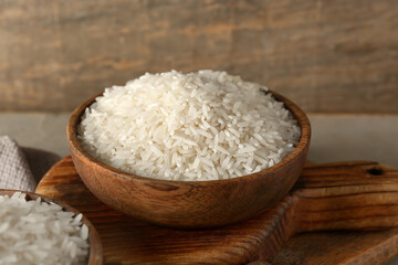 Wooden bowl with raw rice on grey table
