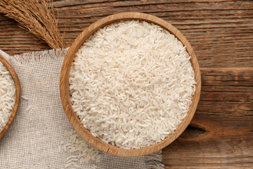 Bowl with raw rice on wooden background