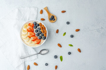 Oatmeal bowl with fruits and spoon and scattered nuts on table