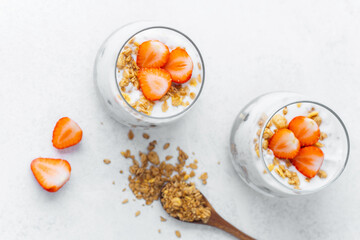 Strawberry yogurt parfait with granola in glass cups on white background, top view, healthy breakfast or dessert concept.