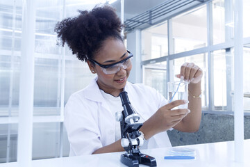 Young american african woman scientist conducting research investigations in a medical development laboratory. researcher student is experiment study and examines a test tube in chemical laboratory.
