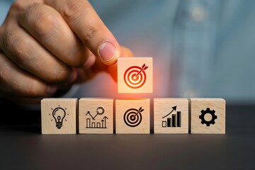 Hand placing a wooden block with a target icon on top of other blocks with business icons