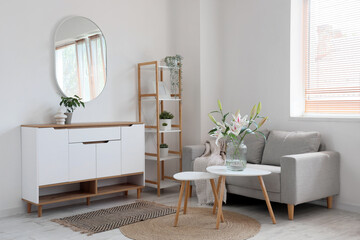 Interior of stylish living room with grey sofa, cabinet and beautiful lily flowers on coffee table