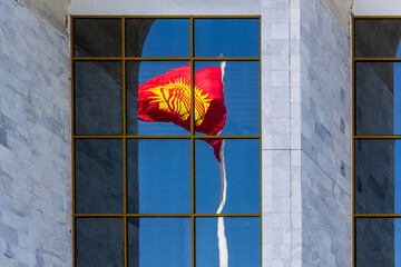 Waving National Flag of Kyrgyzstan reflected in building window under blue sky