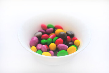 Glazed peanuts of different colors on a plate, white background. Multicolored peanuts. close-up. Snack colored kernel, hazelnut, nut.