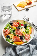 Fresh salad with peaches, arugula, feta, prosciutto and berries in a plate on a light background
