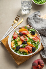 Fresh salad with peaches, arugula, feta, prosciutto and berries in a plate on a wooden board