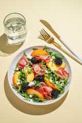Fresh salad with peaches, arugula, feta, prosciutto and berries in a plate on a yellow background