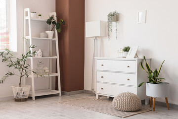 Interior of stylish room with white dresser, shelving unit and standard lamp