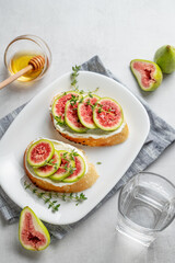 Sweet toasts with fresh figs, cheese, thyme, and honey on a light background.