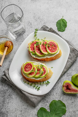 Sweet toasts with fresh figs, cheese, thyme, and honey on a gray background.