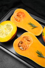 Orange butternut squash halves with rosemary on a black tray, preparing for cooking