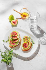 Sweet toasts with fresh figs, cream cheese, thyme, and honey on a marble background.