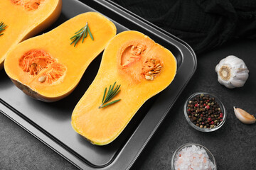 Butternut squash halves with rosemary, peppercorns, garlic and salt on a tray for cooking