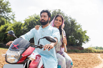 Indian farmer couple riding motorbike in rural farmland