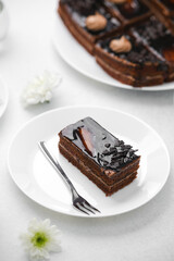 Rich chocolate cake slice with shiny glaze and fork on white plate, close-up view