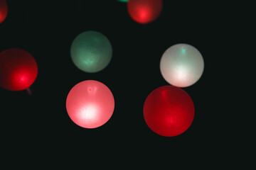 Bright festive round bulbs glow red green and white against dark background