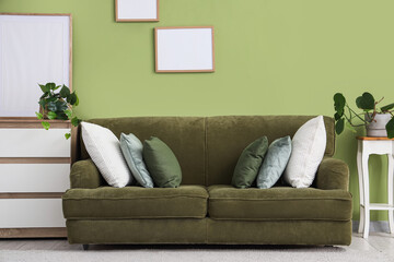 Interior of stylish living room with cozy sofa, dresser and frames near green wall
