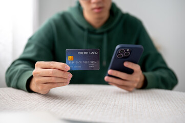 Close up of a man holding or showing a credit card and looking at phone sitting at table in a cafe.
