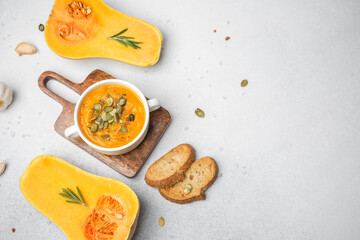 Butternut squash soup with seeds and bread on a wooden board with pumpkin and garlic