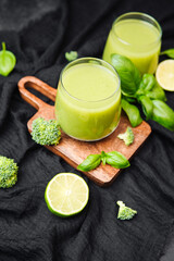 Green smoothie with broccoli and lime on wooden board, fresh basil leaves, healthy drink