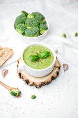 Broccoli soup with fresh basil garnish and whole florets in a bowl on rustic wood base.