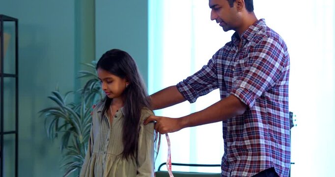 Measuring little daughter&rsquo;s height, Indian father using measuring tape near cupboard in modern home, Asian dad bonding with young girl, family quality time, growth tracking playful indoor activity