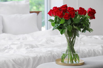 Vase with beautiful red roses on bedside bench in stylish bedroom
