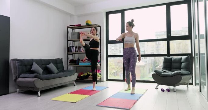 Women train in living room on mats following warmup sequence. Couple raises knees and swings arms stepping in place preparing legs for session