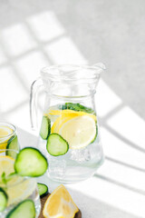 Cucumber lemon water with mint on wooden board in sunlight on white table