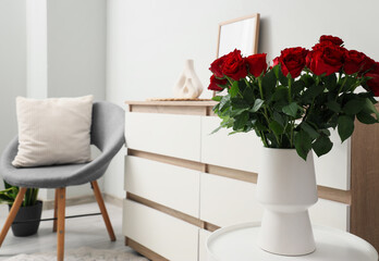 Vase with beautiful red roses on white coffee table in stylish living room, closeup