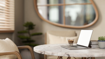 White screen laptop and coffee cup with books on marble table in a garden or living room with bonsai